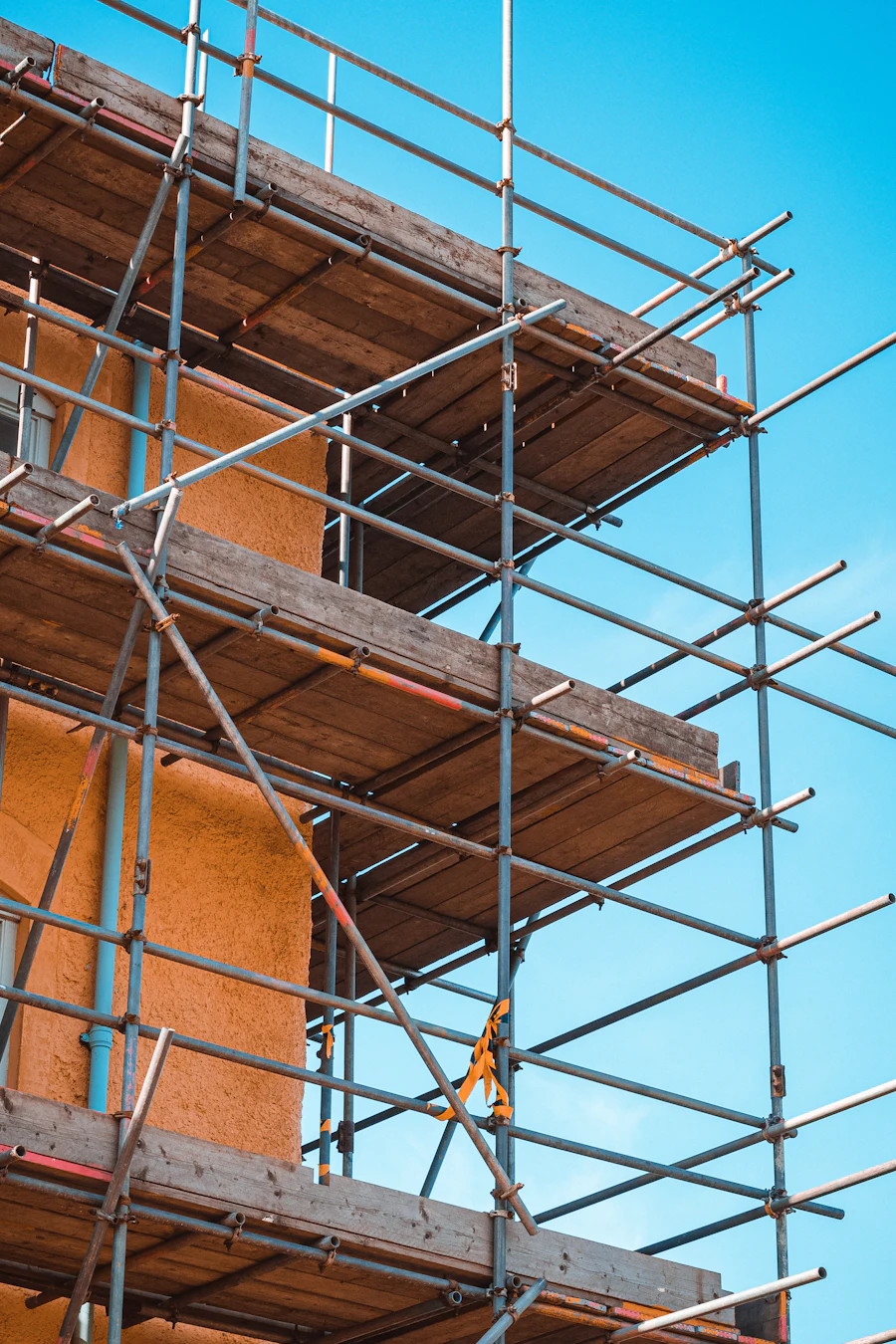 Scaffolding wrapped around a rising building against a bright blue sky