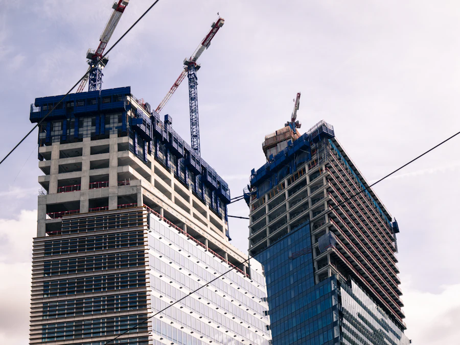 Twin concrete towers rising with tower cranes on their roofs against a pale sky